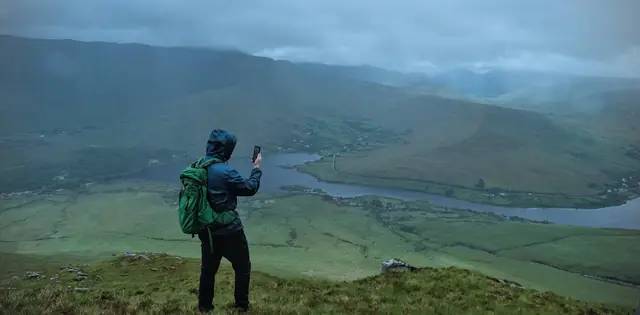 A hiker pausing on a green hillside to take in the valley below