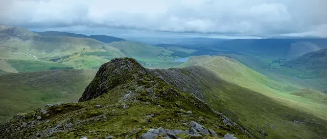 A ridgeline path with green valley and mountains beyond