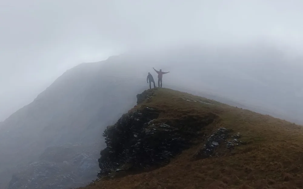 Two hikers celebrating on a rocky ridge in thick mist in the Connemara mountains